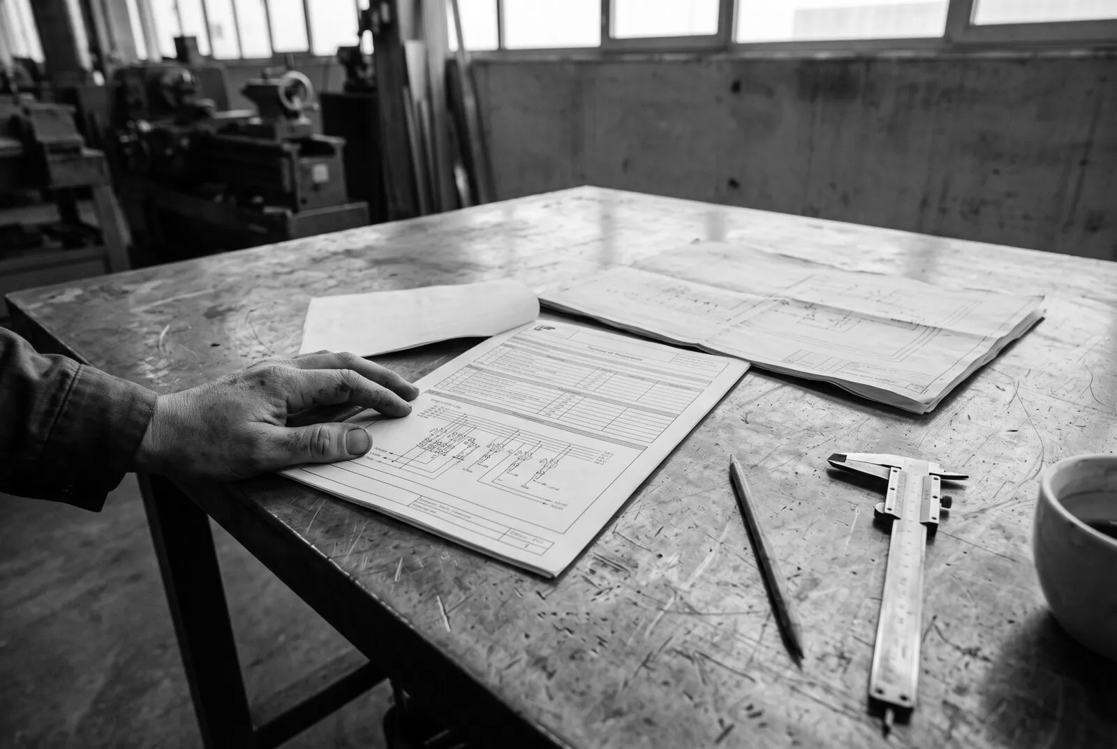 Esquema eléctrico y planos desplegados sobre un banco de trabajo, junto a un pie de metro y un lápiz
